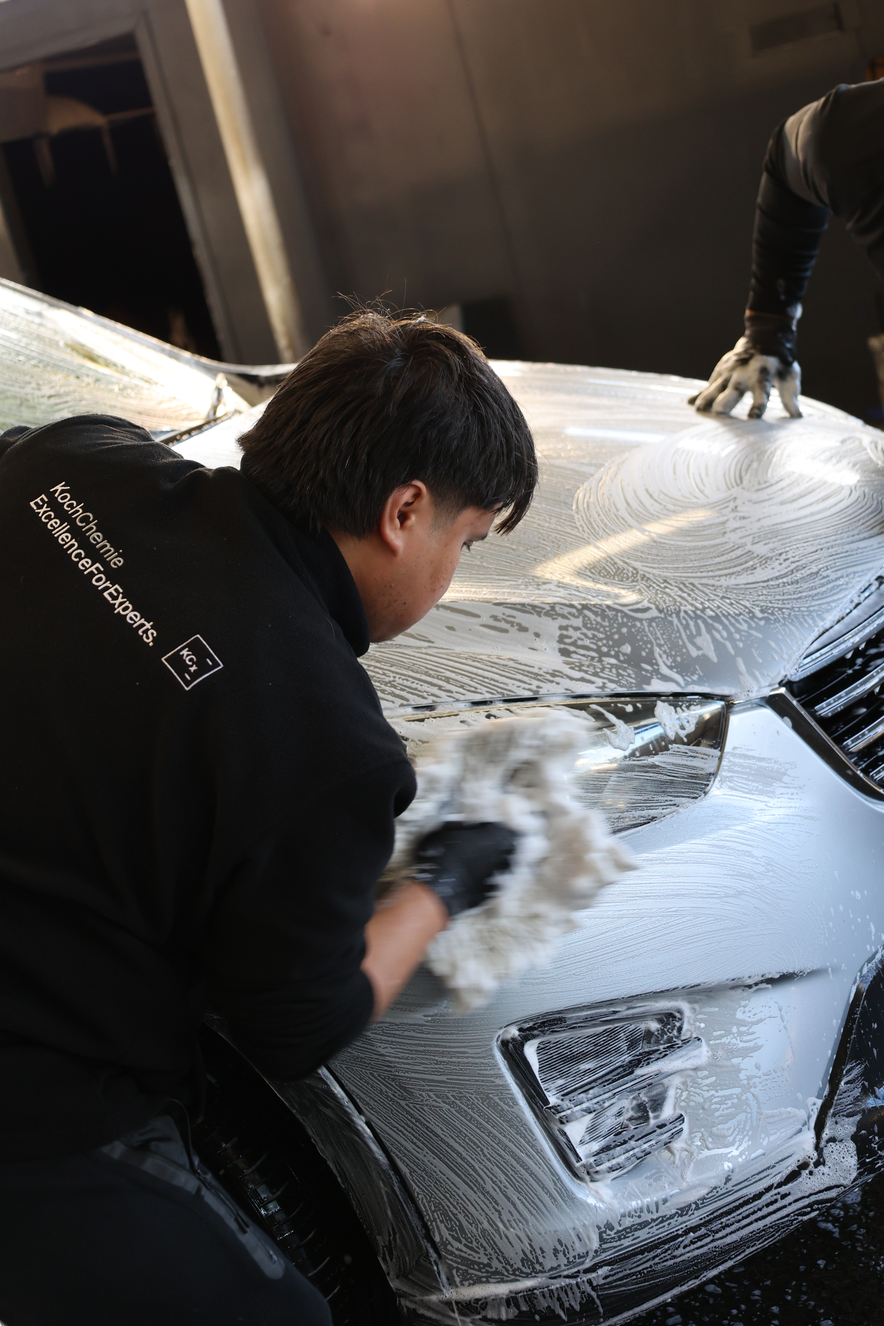 Carfē technician hand-washing a foam-covered car bonnet with a wash mitt