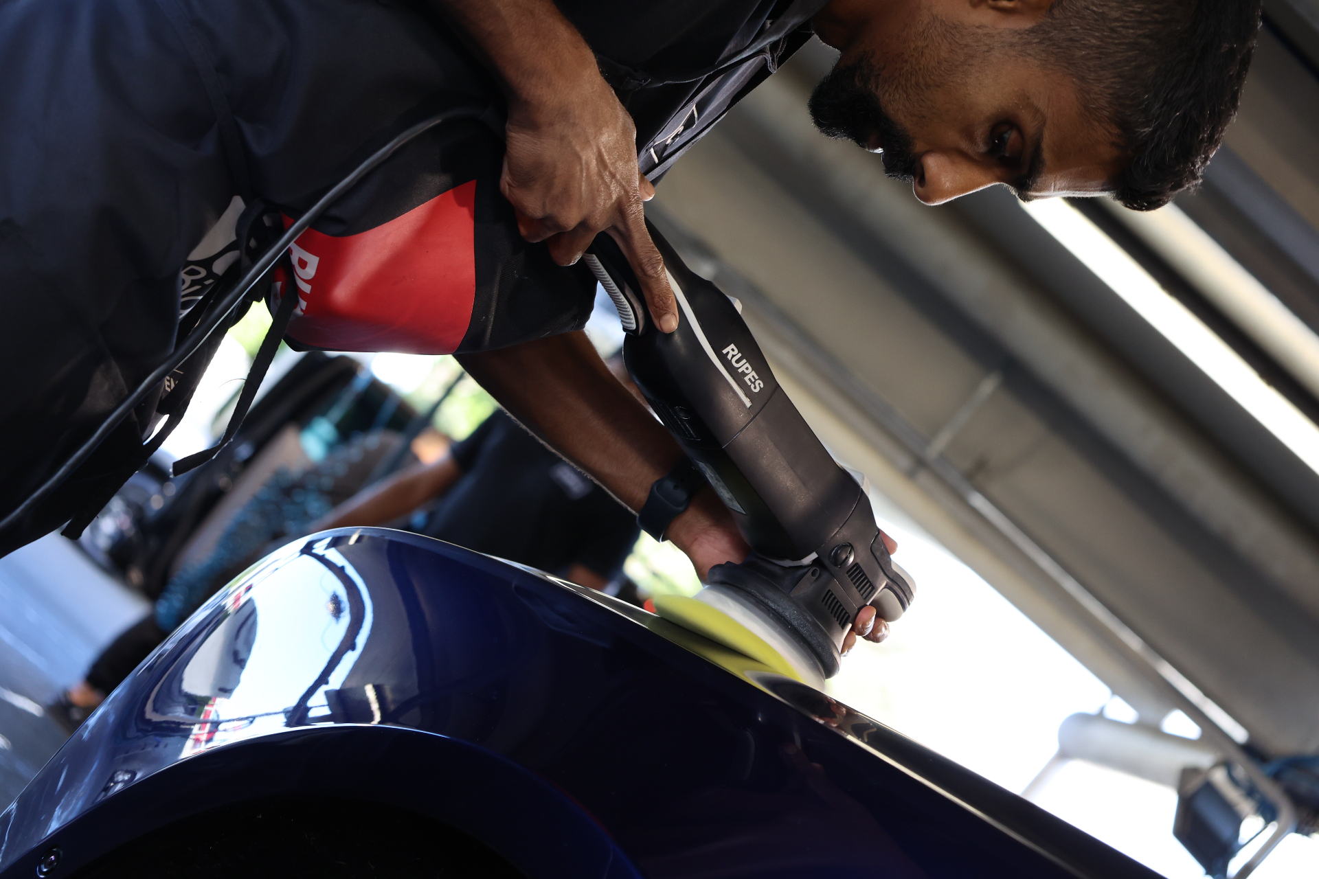 Detailer machine-polishing a deep blue panel with a Rupes polisher